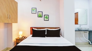 Een hotelkamer met een bed, nachtkastje met een lamp, telefoon en een badkamer met wastafel en spiegel.
