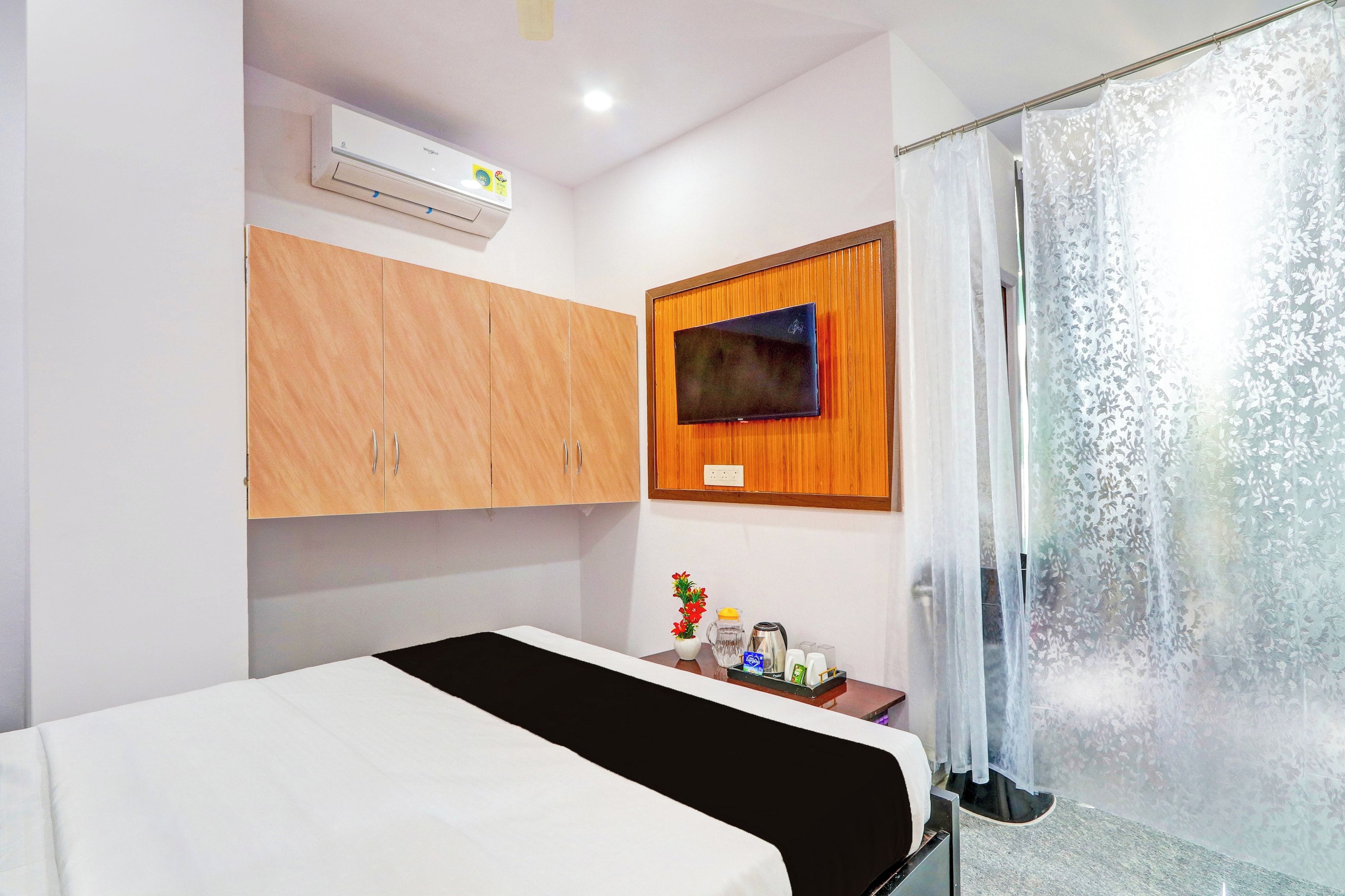 Een hotelkamer met een bed, een flatscreen televisie bevestigd aan een houten paneel, een klein tafeltje met toiletartikelen en een douche met ruitverdelende glazen deuren.