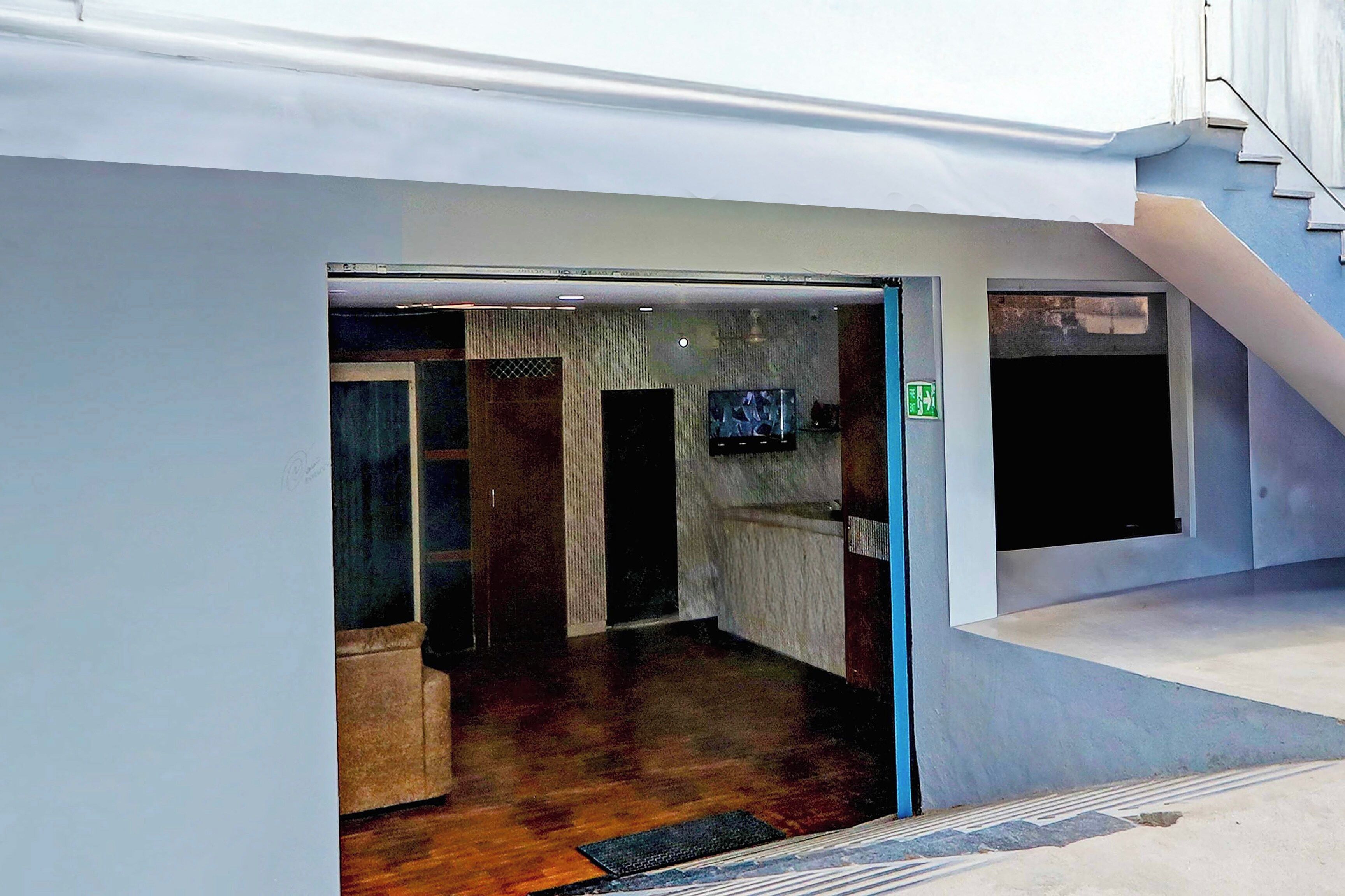 A modern interior with a glass door entrance, a staircase, and a flat-screen TV mounted on the wall.