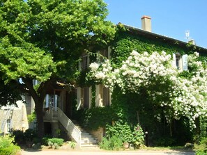 Een historisch gebouw met een gevel van natuursteen, een overdekte veranda en een trap naar de ingang.