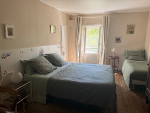A bedroom with a bed, a chair, a table, and a window with curtains.