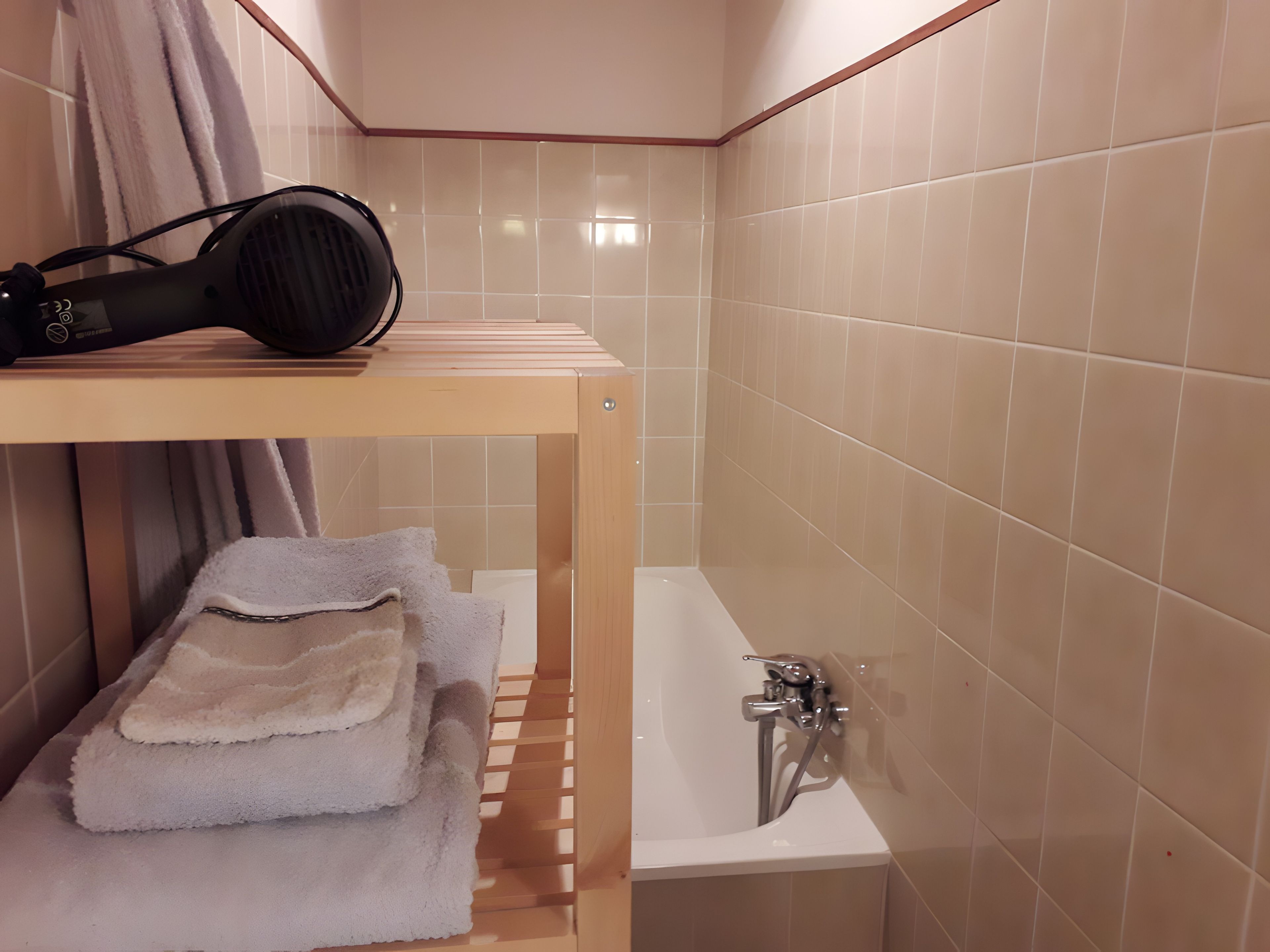 Ein Badezimmer mit einer Badewanne, einem Handtuchhalter mit Handtüchern und einem Fön auf dem Ablagefach.