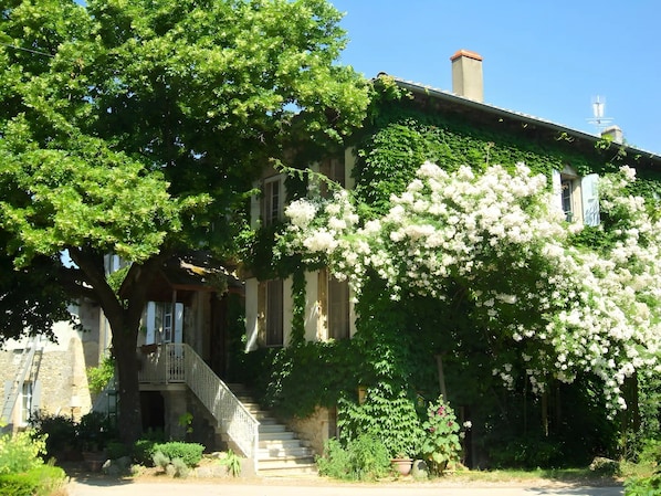 A historic building with a stone facade, a covered porch, and a staircase leading to the entrance.