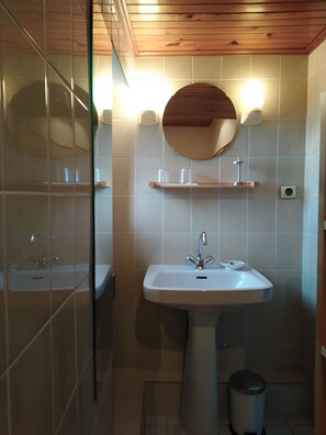 Een badkamer met een wastafel op een voetstuk, een ronde spiegel en twee wandlampen.
