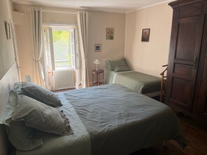 Een slaapkamer met een bed, een stoel, een radiator en een raam met gordijnen.