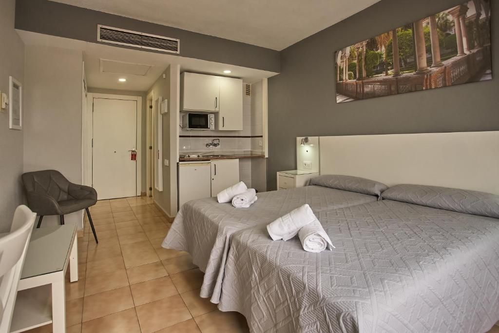Una habitación de hotel con cama, escritorio, silla, microondas y un cuadro en la pared.