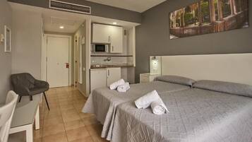 Una habitación de hotel con cama, escritorio, silla, microondas y un cuadro en la pared.