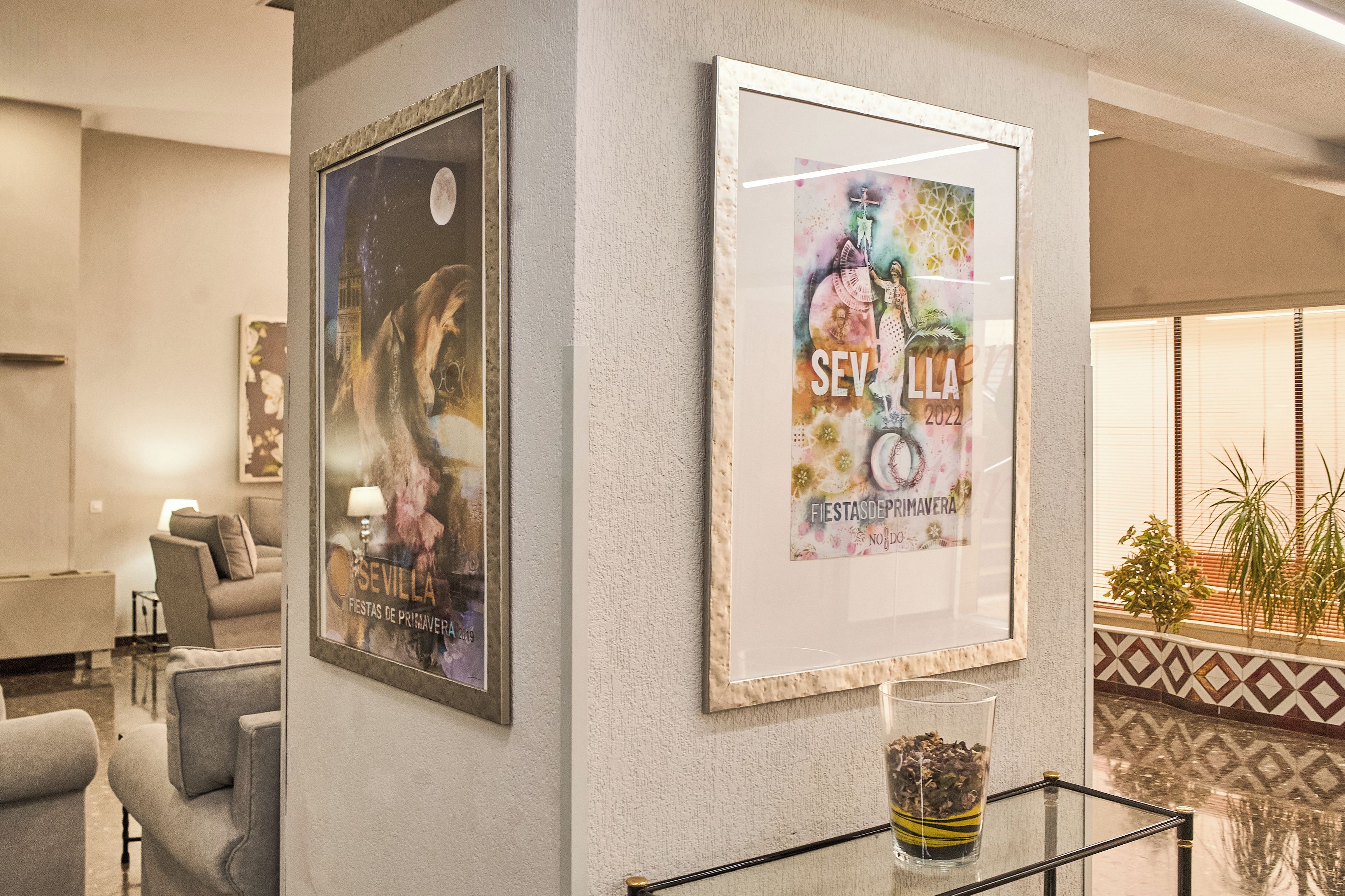 A hotel lobby with framed posters on the wall, a glass table with a decorative item, and a patterned floor.