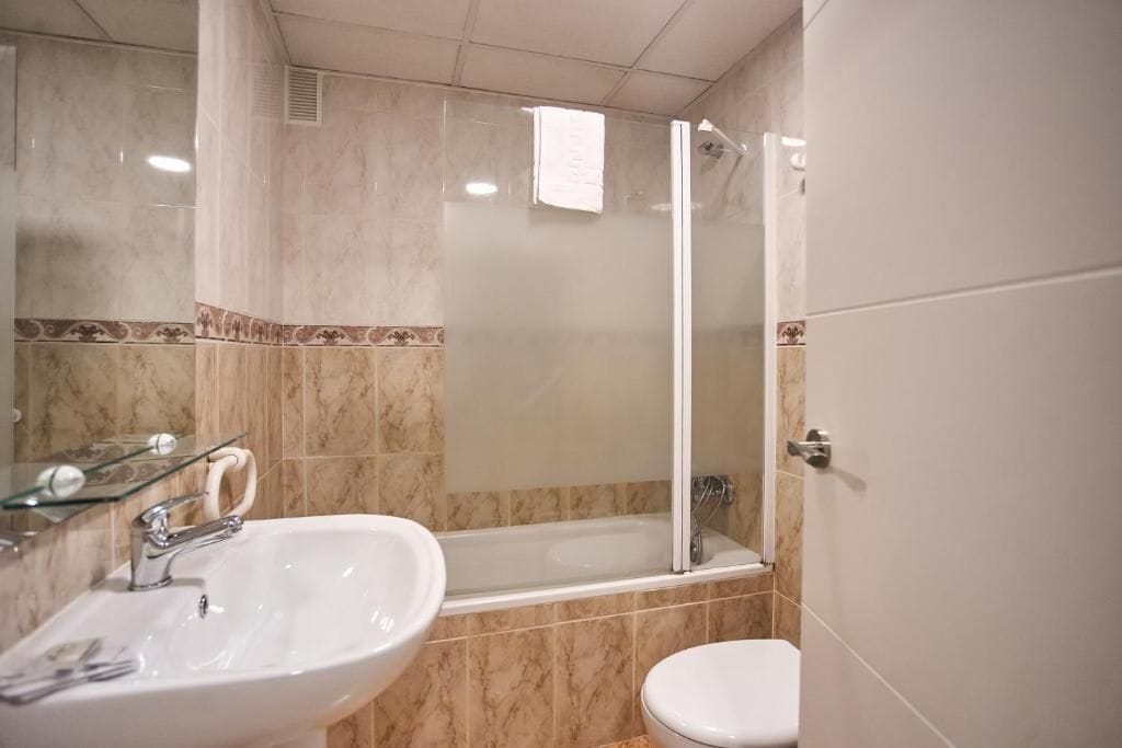 A bathroom with a glass-enclosed shower, a white sink, and a toilet.