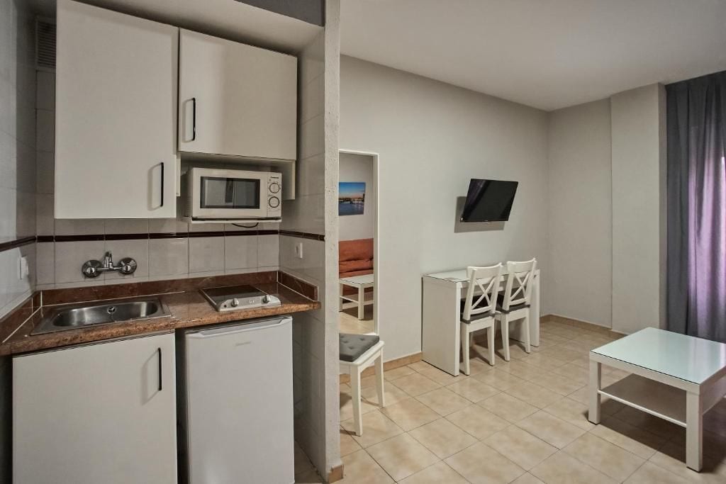 A compact kitchen with a microwave, sink, and refrigerator. There is a small dining area with a table and chairs.