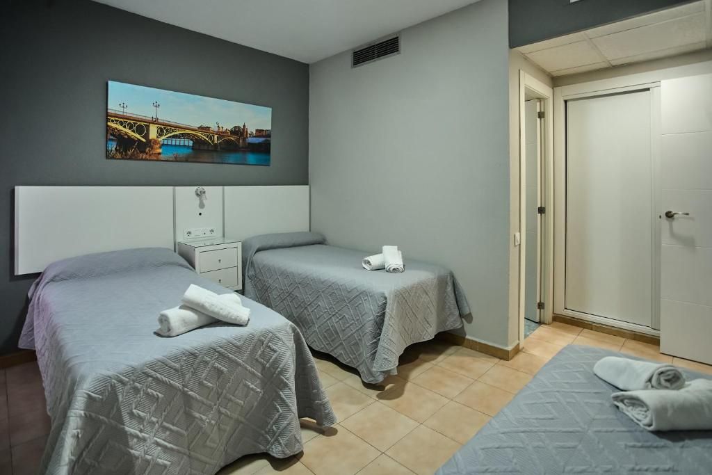 Habitación de hotel con dos camas, un cuadro de un puente, una puerta blanca y suelo de baldosas.
