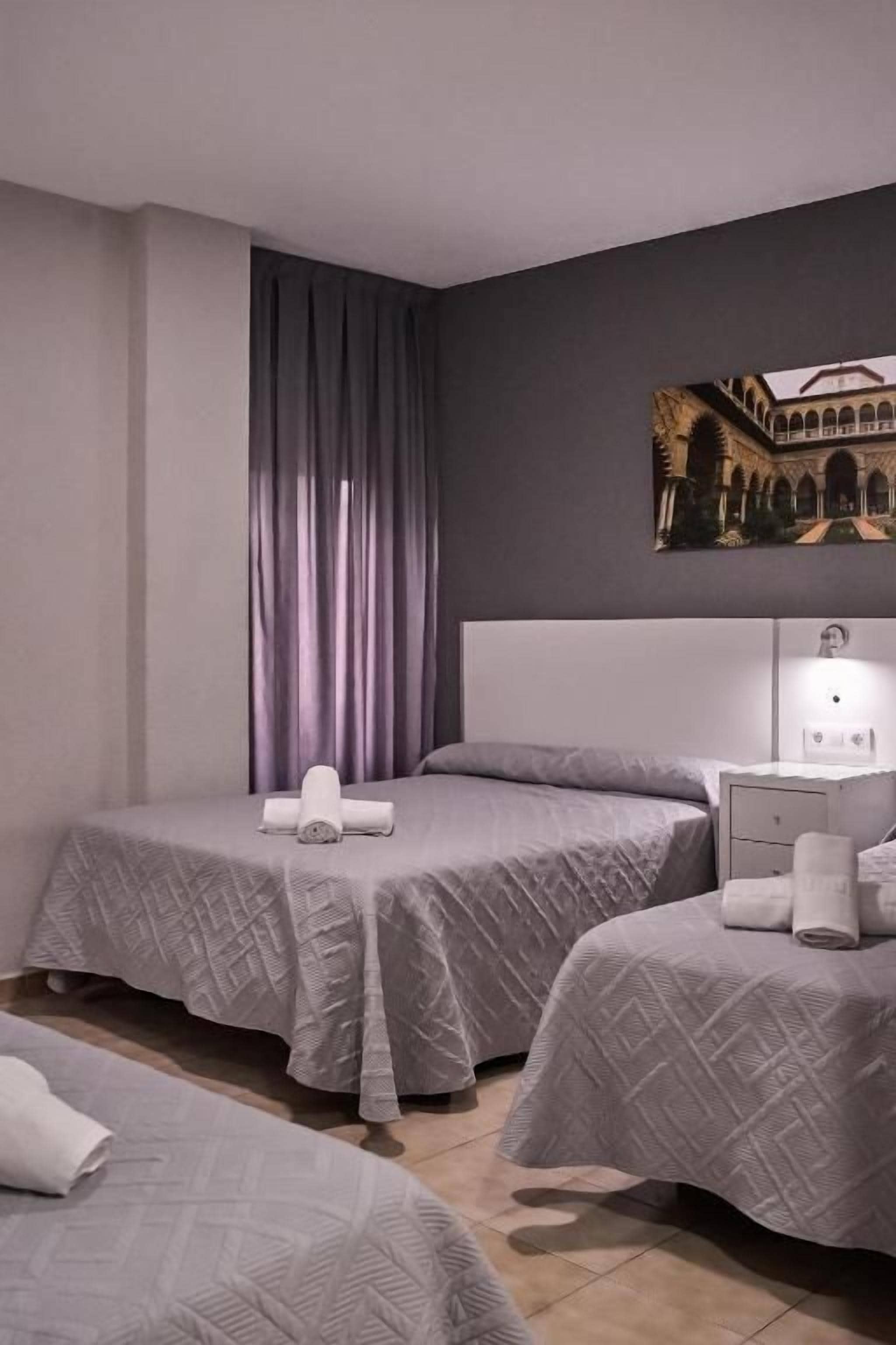 Una habitación de hotel con dos camas, una mesita de noche, una lámpara y un cuadro en la pared.
