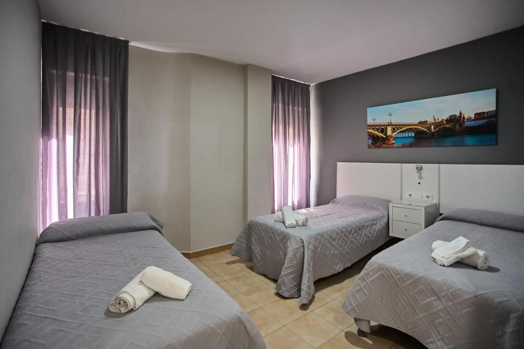 Quarto de hotel com duas camas de solteiro, uma mesinha de cabeceira, uma TV na parede e um quadro de uma ponte.