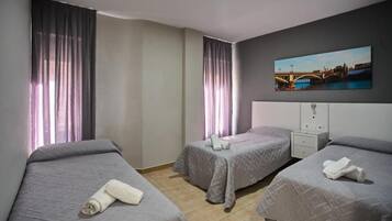 Quarto de hotel com duas camas de solteiro, uma mesinha de cabeceira, uma TV na parede e um quadro de uma ponte.