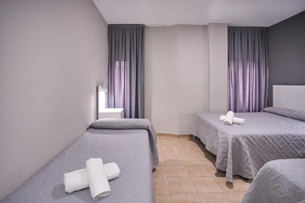 Una habitación de hotel con dos camas, un ventanal con cortinas y suelo de baldosas.