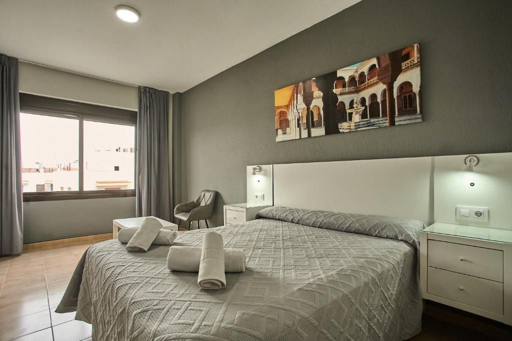Una habitación de hotel con una cama grande, una silla, una mesita de noche y un cuadro en la pared.