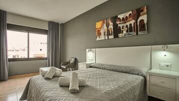 Una habitación de hotel con una cama grande, una silla, una mesita de noche y un cuadro en la pared.