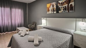 Una habitaci ón de hotel con cama, una silla, una mesita y una mesita de noche.