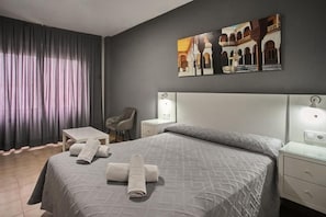 Quarto de hotel com cama, poltrona, mesa pequena e criado-mudo.