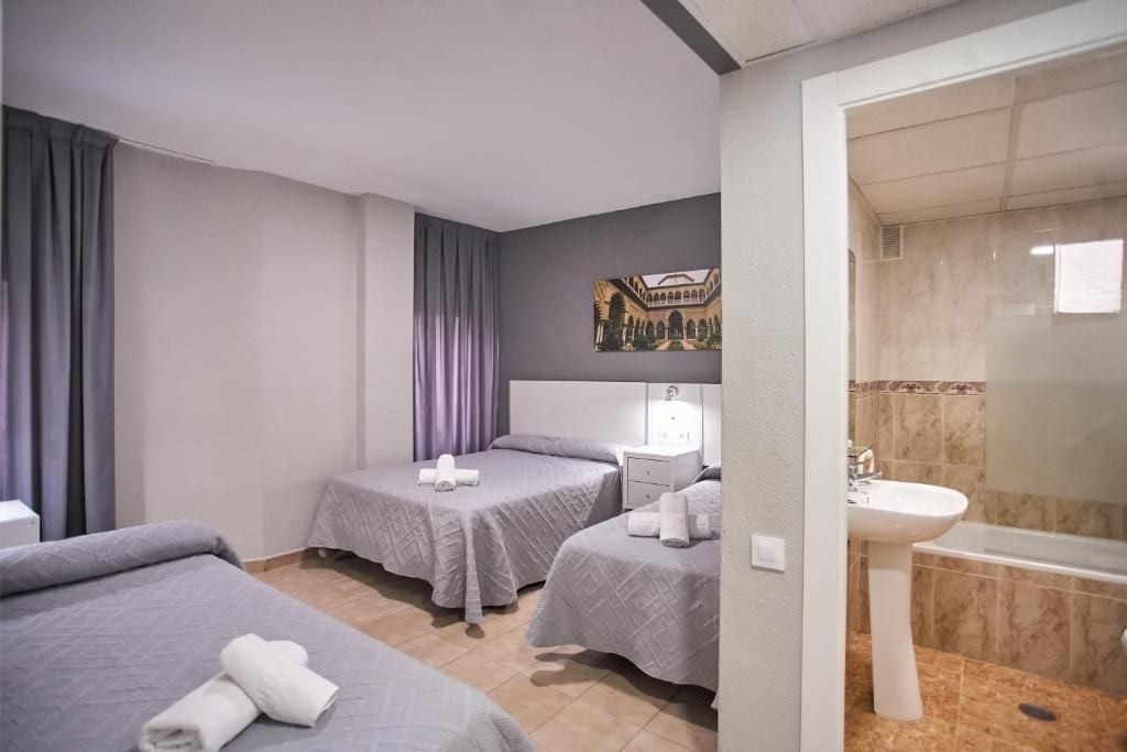 Habitación de hotel con dos camas, baño con lavamanos y bañera, y un cuadro en la pared.