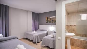 Habitación de hotel con dos camas, baño con lavamanos y bañera, y un cuadro en la pared.