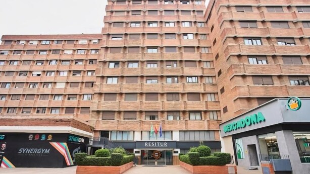 Un edificio de varios pisos con una planta baja comercial, que cuenta con un gimnasio, un supermercado Mercadona y un restaurante llamado Resitur.