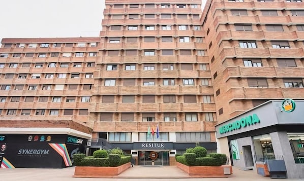 Edifício com vários andares, com área comercial no térreo, que inclui uma academia, um supermercado Mercadona e um restaurante chamado Resitur.
