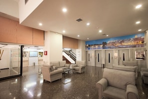 Um hall com assentos, escadaria e um mural de uma paisagem urbana.