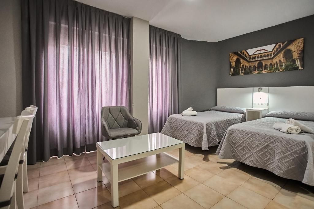 A hotel room with two beds, a chair, a table, and a painting on the wall.