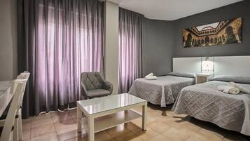 A hotel room with two beds, a chair, a table, and a painting on the wall.