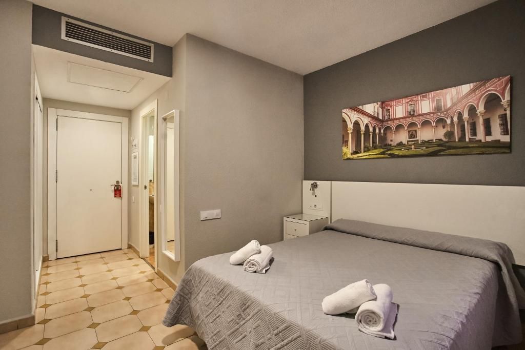 A hotel room with a bed, a painting, a nightstand, and a door.