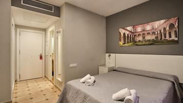 A hotel room with a bed, a painting, a nightstand, and a door.