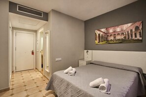 A hotel room with a bed, a painting, a nightstand, and a door.
