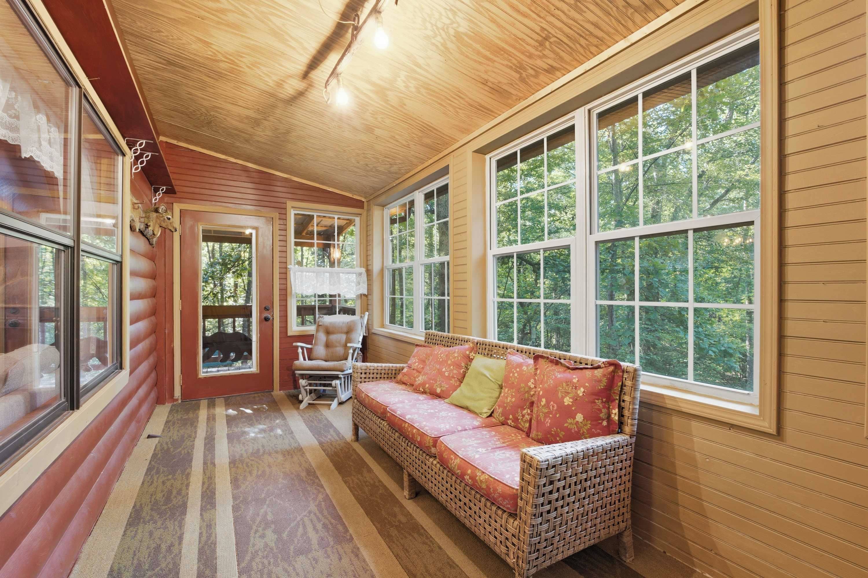 A cozy room with a wicker sofa, a rocking chair, and large windows offering a view of the outdoors.