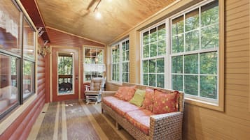 A cozy room with a wicker sofa, a rocking chair, and large windows offering a view of the outdoors.
