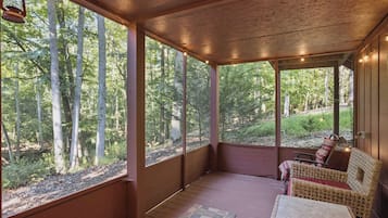 A covered porch with a view of a forest, wicker furniture, and a table.