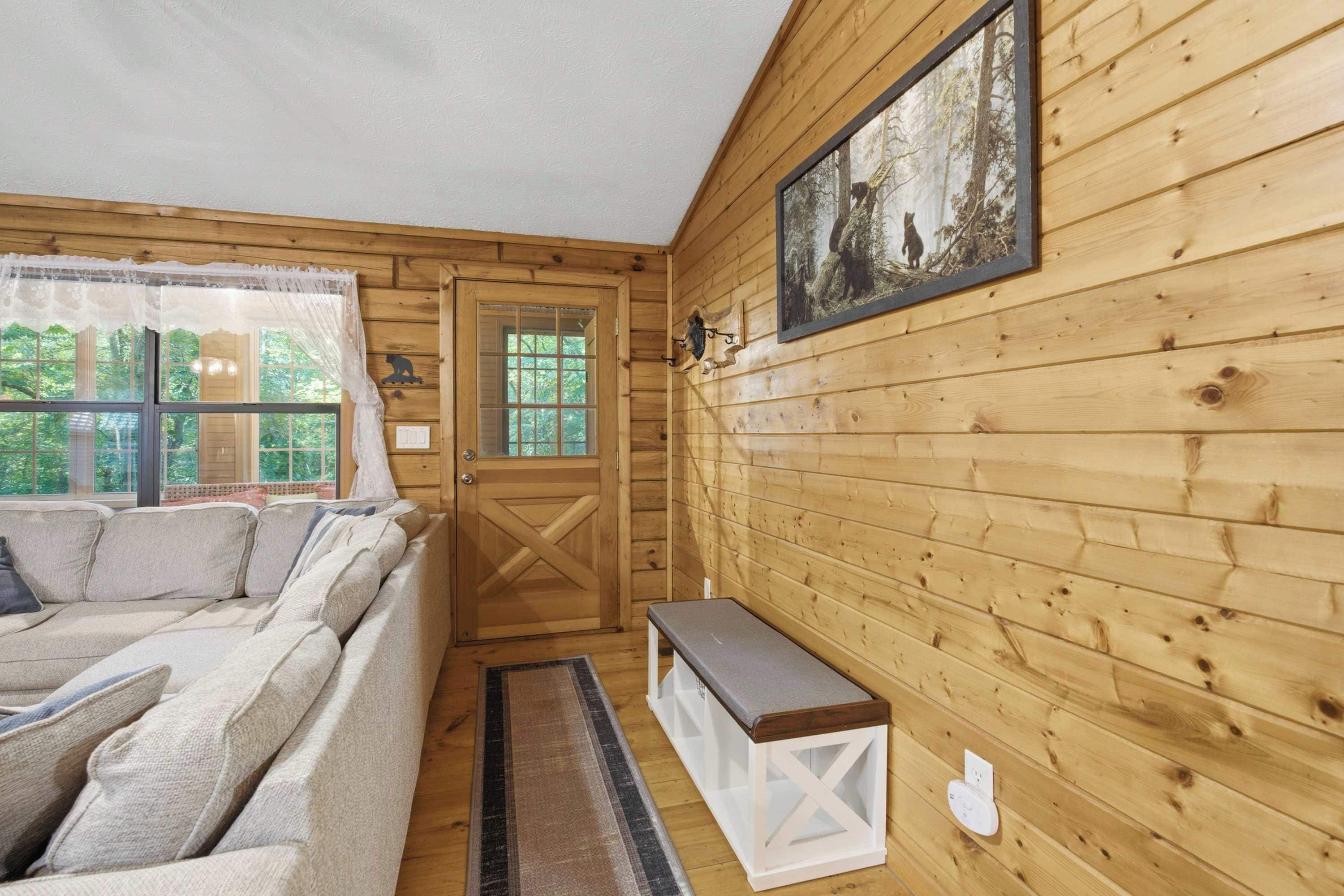 A cozy cabin interior with a wooden exterior, a sofa, a bench, and a framed picture on the wall.