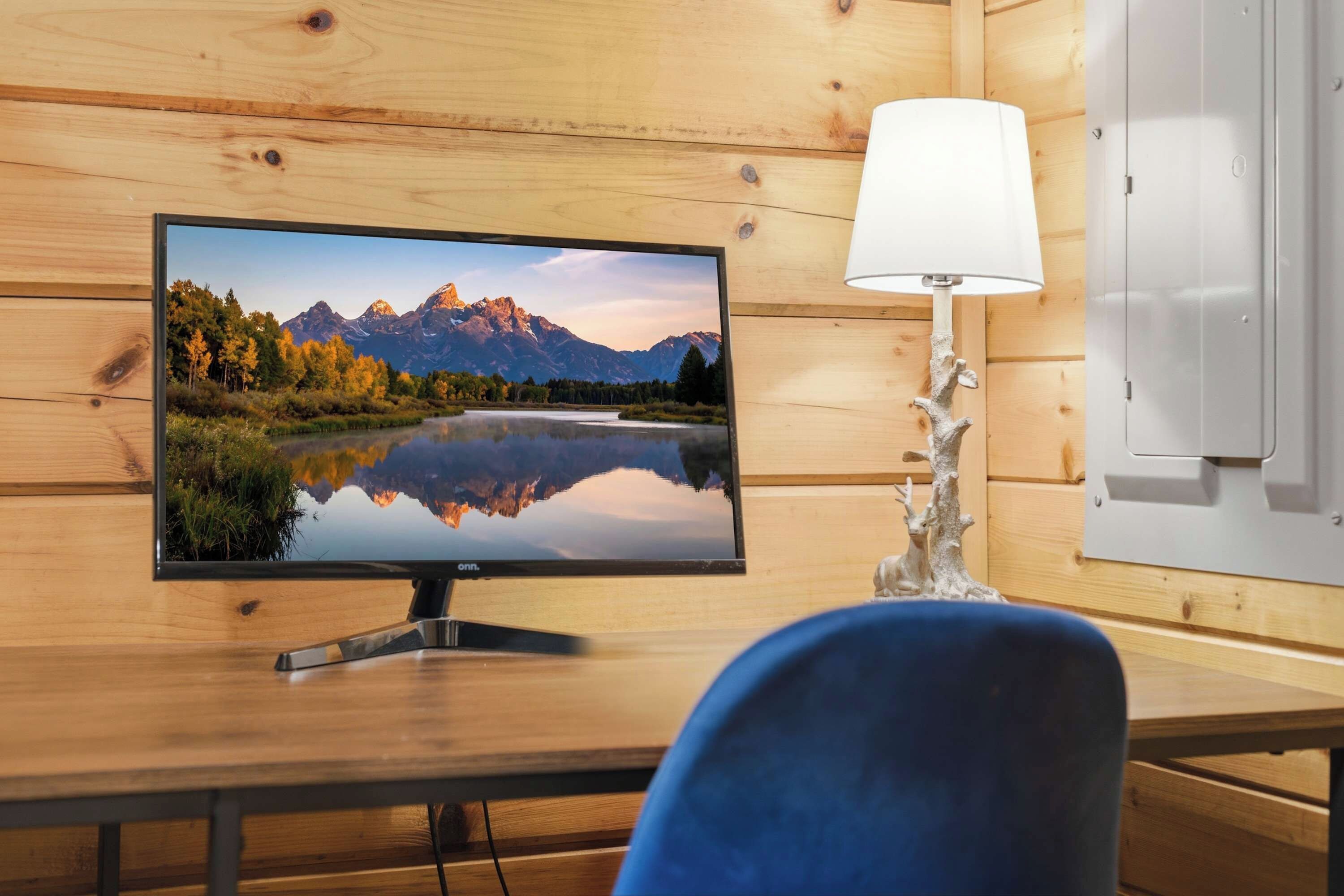 A wooden-framed room with a flat-screen TV displaying a mountain landscape, a white lamp, and a blue chair.