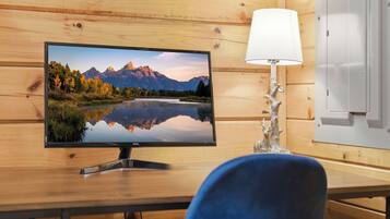 A wooden-framed room with a flat-screen TV displaying a mountain landscape, a white lamp, and a blue chair.