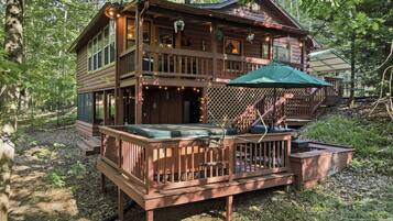 A cabin with a deck, outdoor seating, and a staircase leading to an upper level.