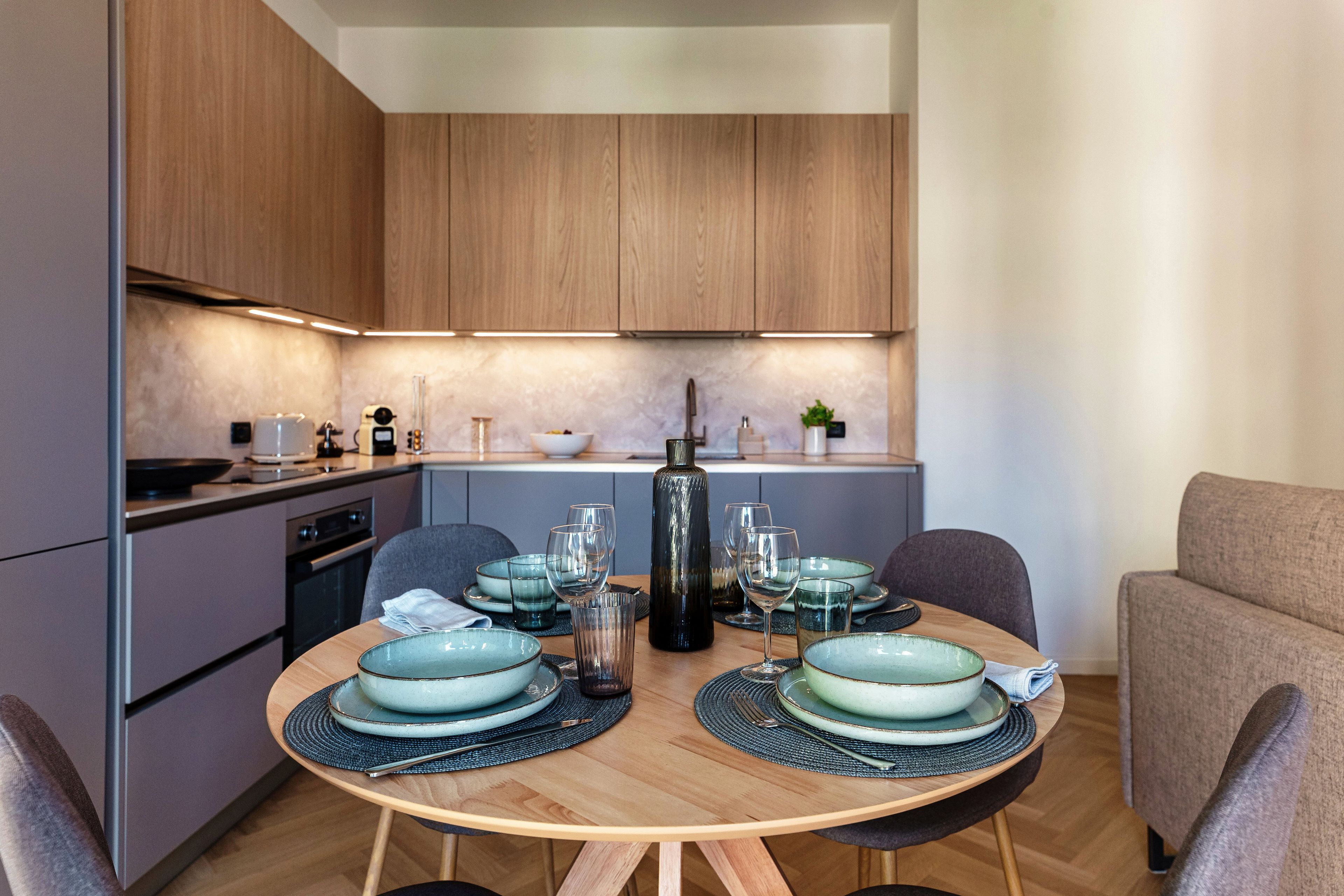 A modern kitchen with wooden cabinets, a dining table set with plates, glasses, and cutlery.