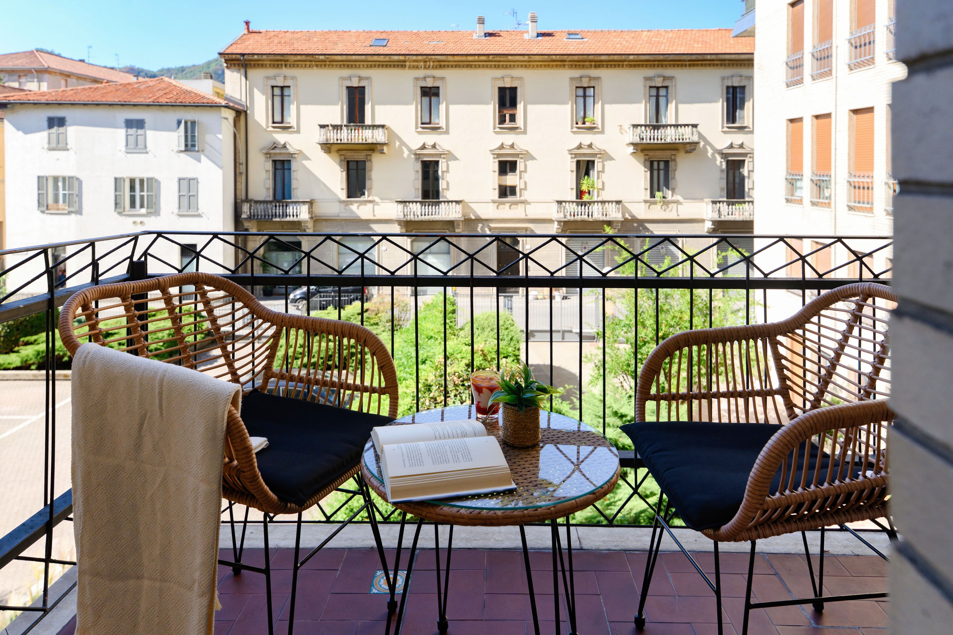 Un balcone con sedie in vimini, un tavolino e un libro.