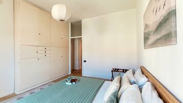A bedroom with a bed, a wardrobe, a hanging light fixture, and a painting on the wall.