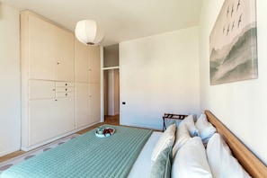 Un dormitorio con cama, armario, lámpara colgante y un cuadro en la pared.