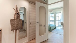A room with a wooden floor, a bed with a green blanket, a chair, and a door leading to another room. - Otium Lake Como (Como)
