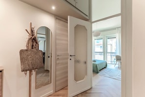 A room with a wooden floor, a bed with a green blanket, a chair, and a door leading to another room. - Otium Lake Como (Como)