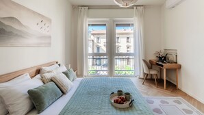 A bedroom with a bed, a desk, a chair, and a balcony with a view of buildings. - Otium Lake Como (Como)