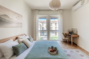 A bedroom with a bed, a desk, a chair, and a balcony with a view of buildings. - Otium Lake Como (Como)