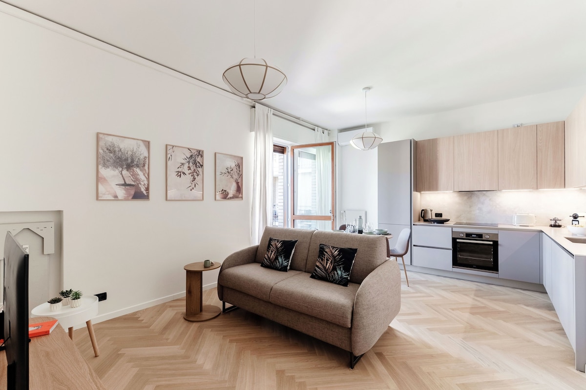 A modern living room with a sofa, a dining table, and a kitchen area with cabinets and appliances.
