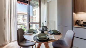 A dining area with a table set for two, a view of the outside, and a kitchen area with a kettle and a coffee maker. - Otium Lake Como (Como)